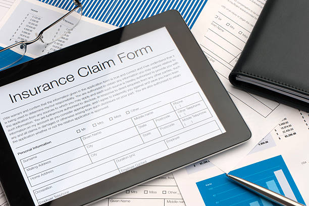 A person filling out an insurance claim form with a pen.